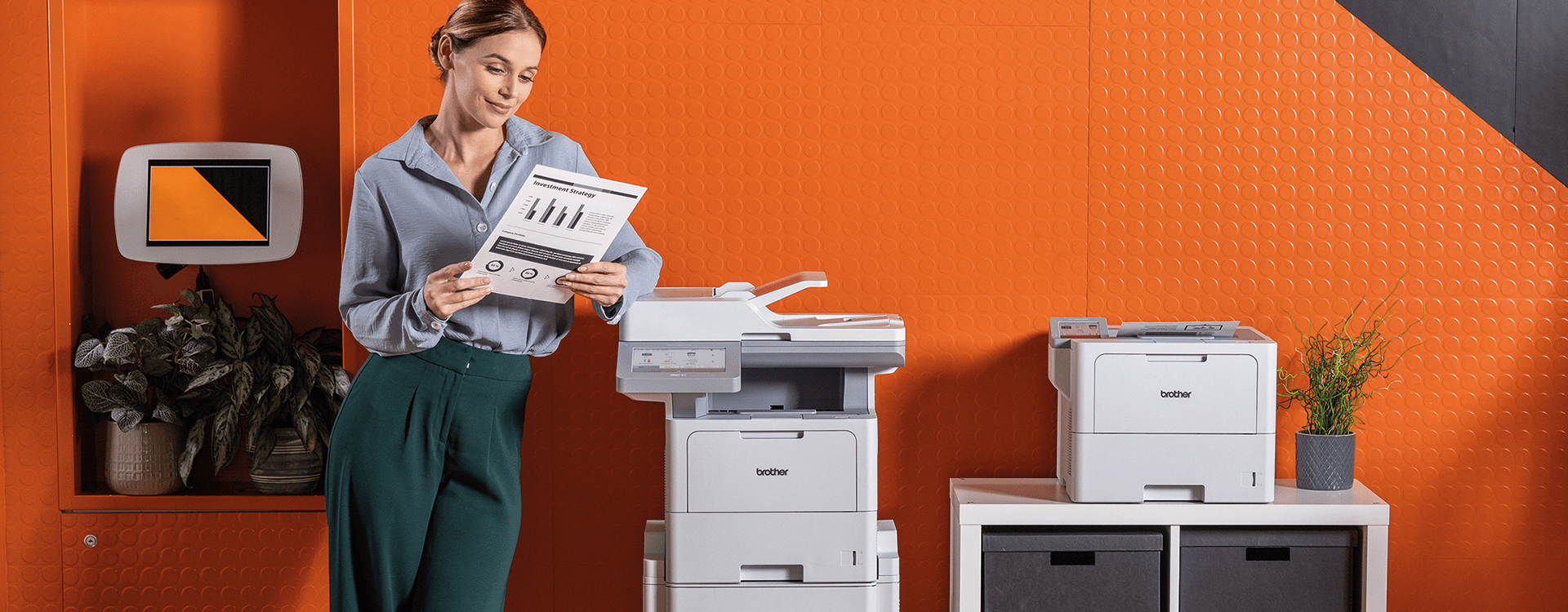 A woman stands beside a printer and a computer, engaged in her work in a modern office environment. Brother Gulf, Middle East & Africa