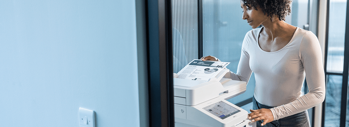 A woman operates a printer in a modern office setting, focused on her task amidst a professional environment. Brother Gulf, Middle East & Africa